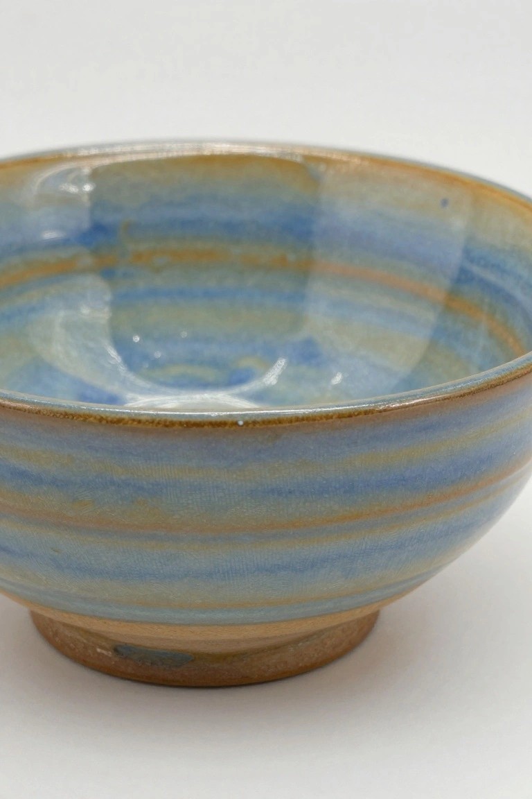 Footed ceramic bowl with swirling blue and orange-brown glaze patterns on a white background.