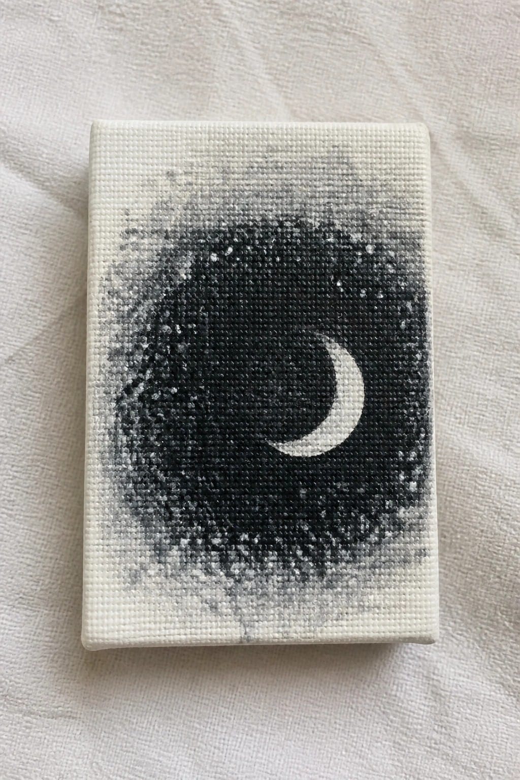 Small canvas with black starry sky and white crescent moon on white fabric.