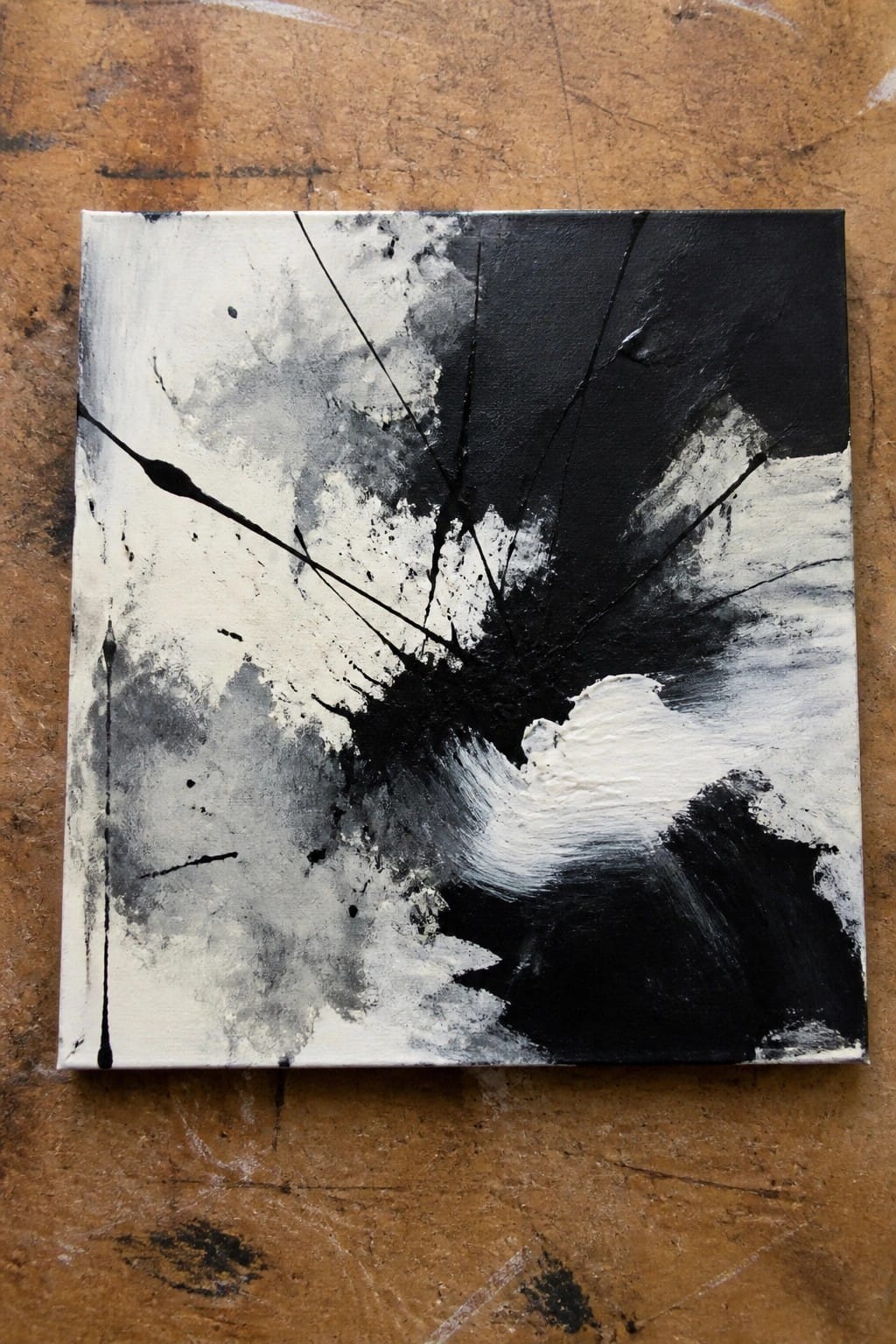 Abstract black and white painting with splatters and drips on wooden surface