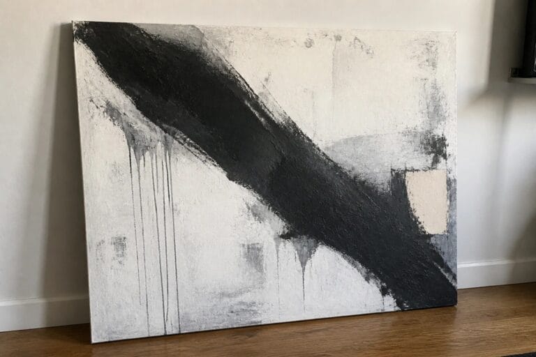 Abstract black-and-white painting with diagonal strokes and drips leaning on wooden floor against wall