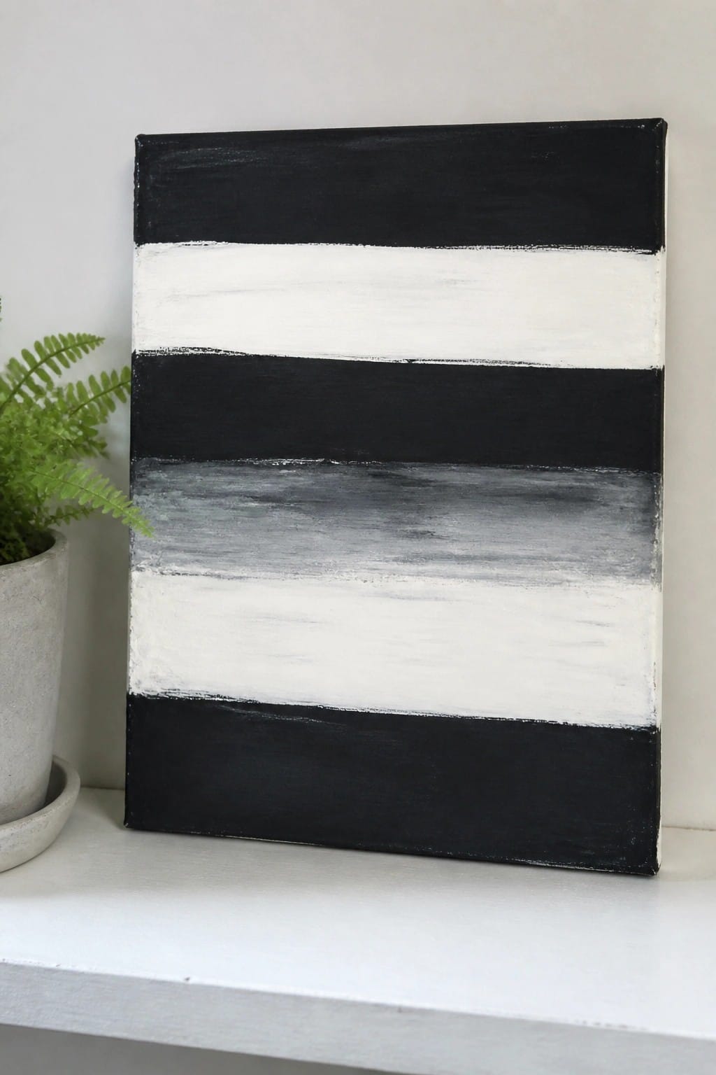 Black white and gray horizontal striped abstract painting beside potted fern plant
