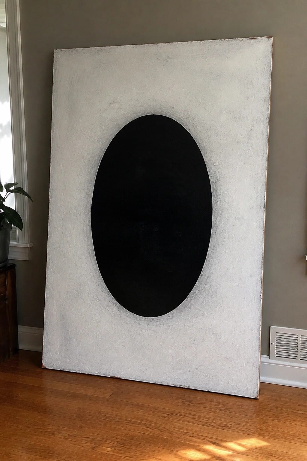 Large abstract painting with textured white background and centered black oval against wall