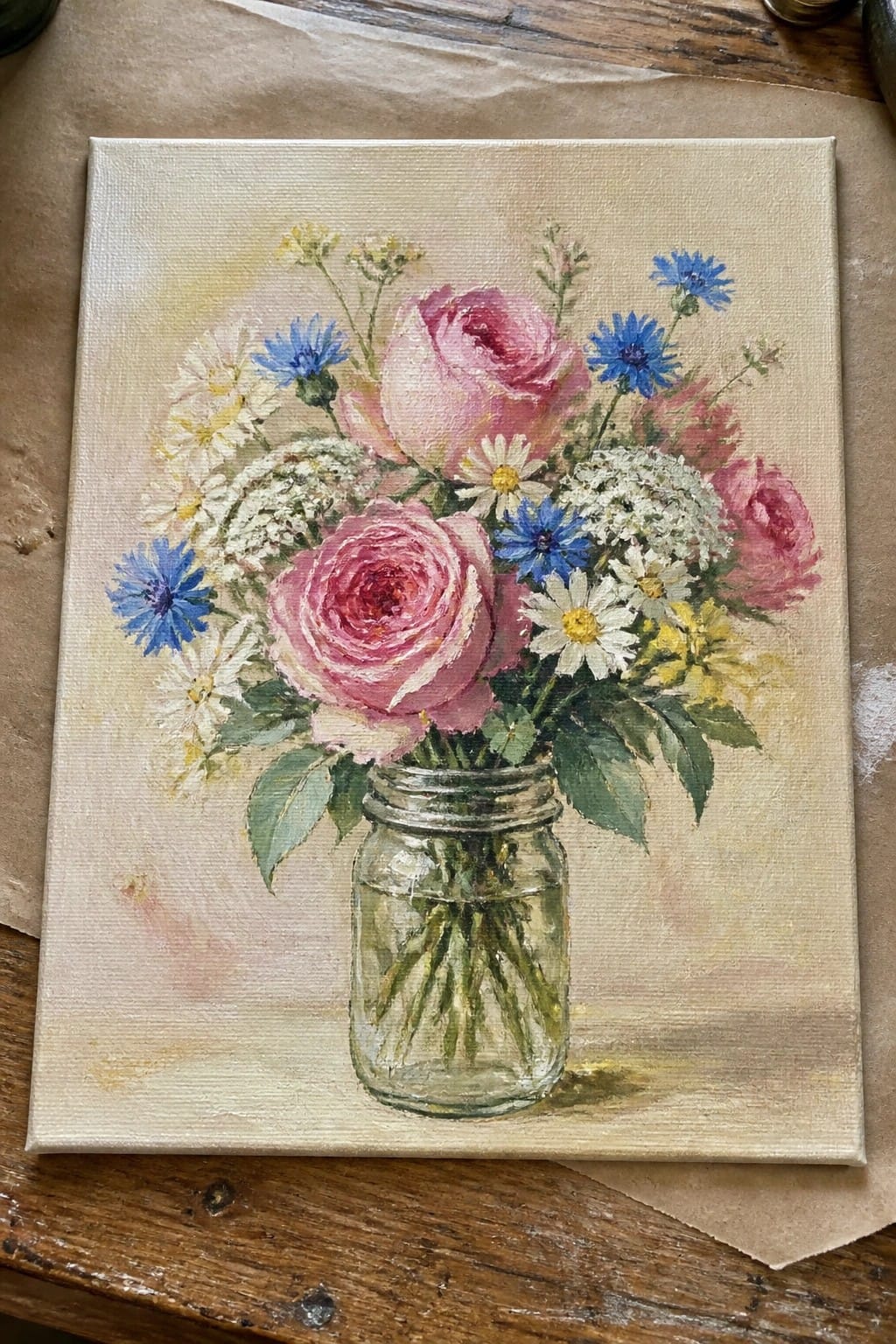 Oil painting of pink roses, blue cornflowers, and daisies in a glass mason jar
