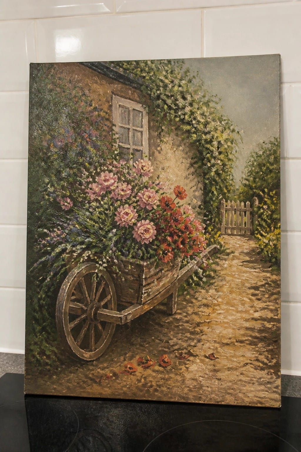 Wheelbarrow brimming with pink roses and red flowers on a path by a cottage.