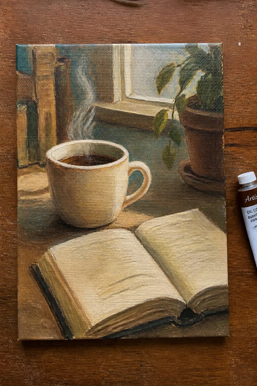 Steaming coffee mug beside open book on wooden table with plant and window light