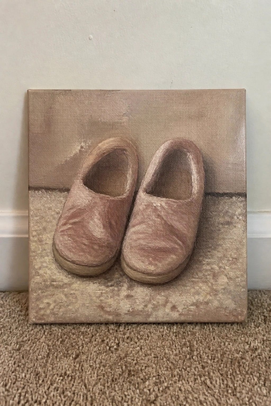 Two pink clogs painted on a square canvas leaning against a wall