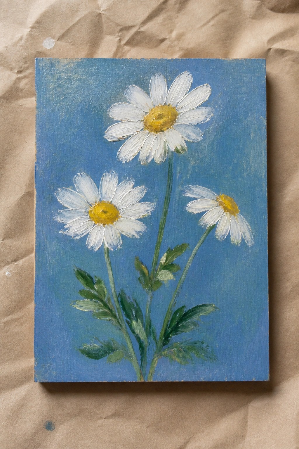 Three white daisies with yellow centers on green stems against blue background on brown paper