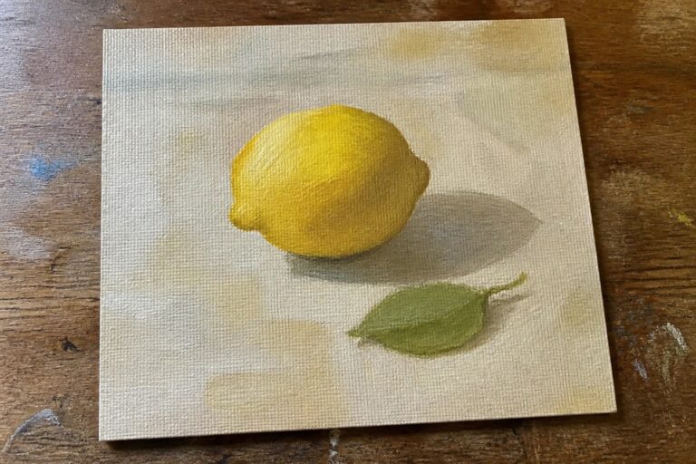 Yellow lemon and green leaf painted on square canvas atop wooden table