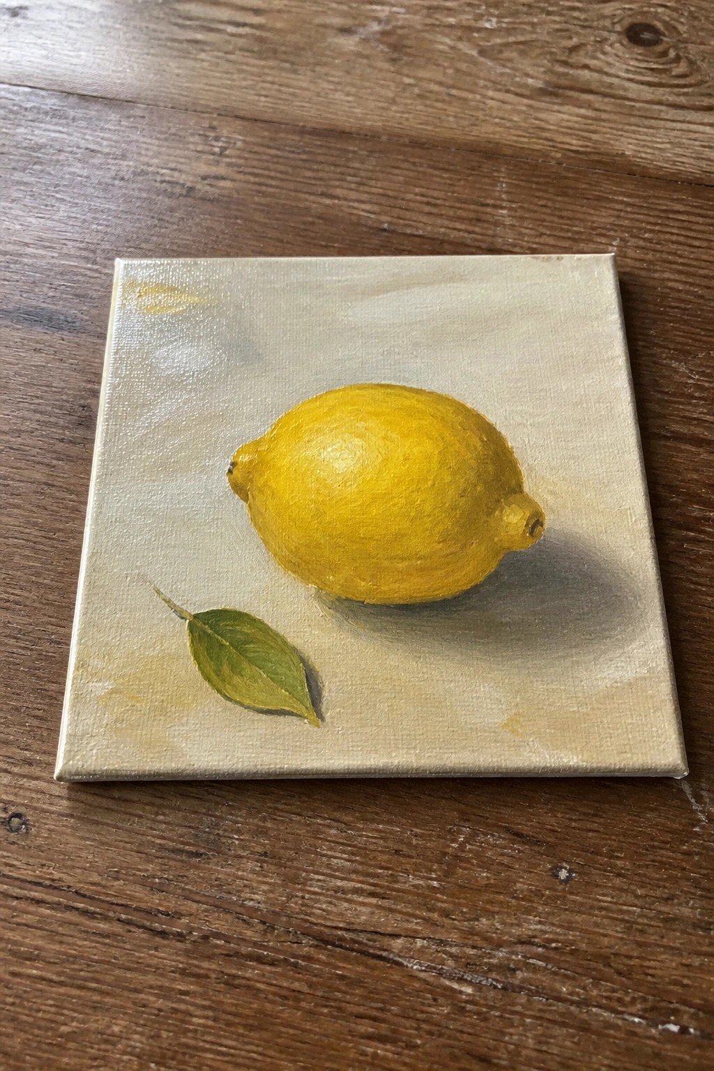 Yellow lemon and green leaf painted on square canvas atop wooden table