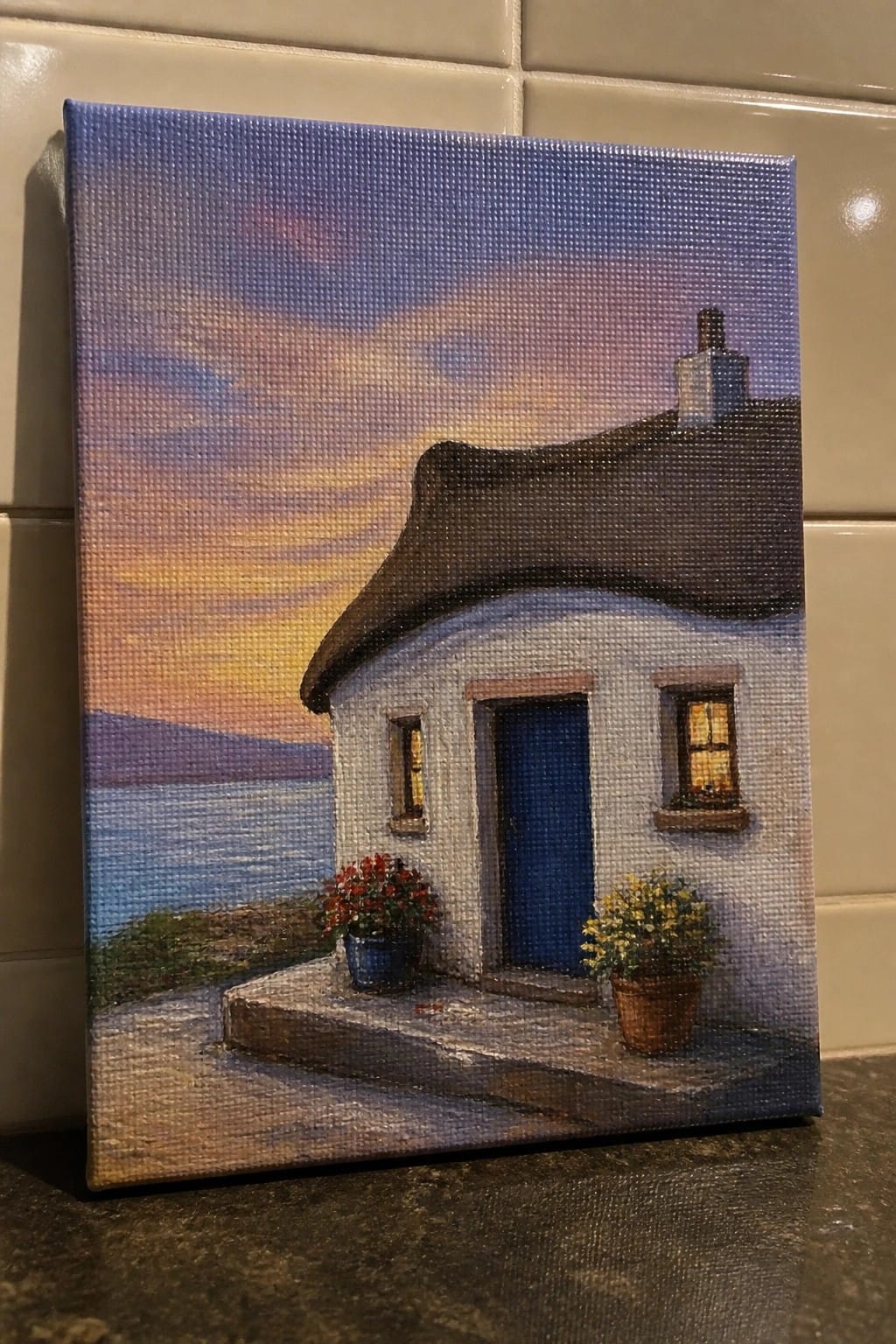 White thatched cottage with blue door and flower pots by sea at sunset