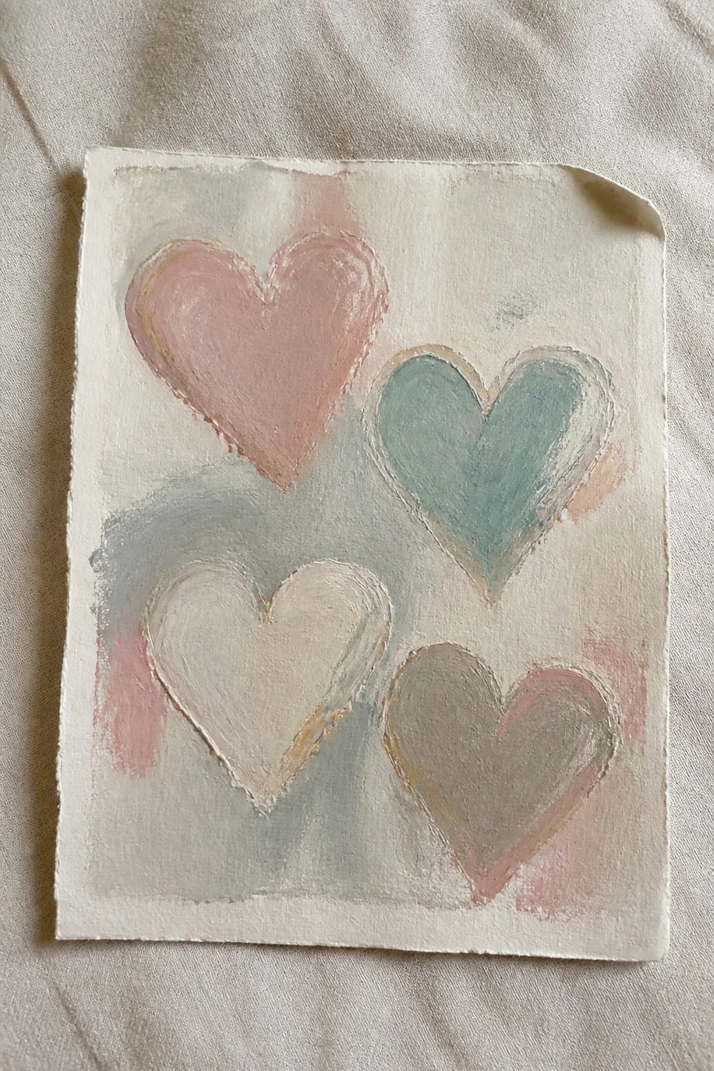 Four pastel hearts painted in pink, teal, cream, and taupe on paper.