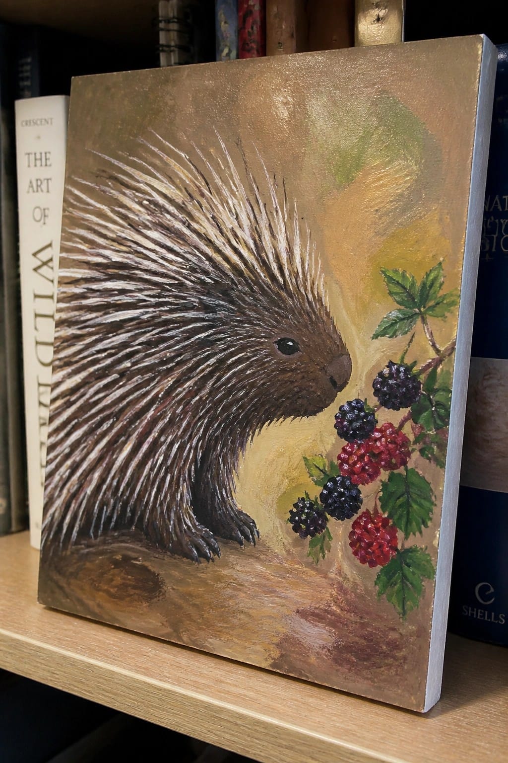 Porcupine painting with spiky quills and berry branch on gold canvas beside books