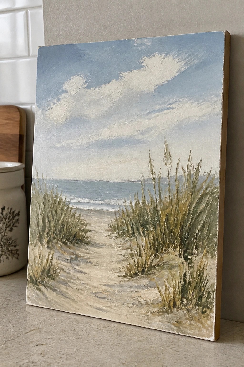 Beige sand path through green sea grass to blue ocean in landscape painting on countertop.