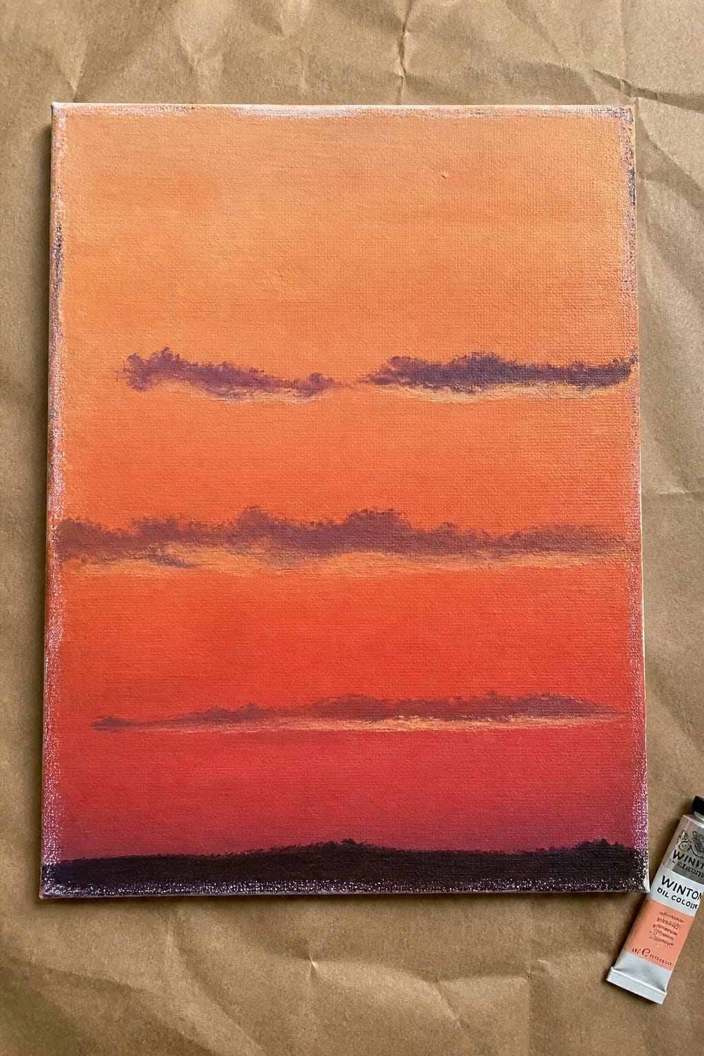 Orange-red gradient canvas painting with dark streaks beside oil paint tube