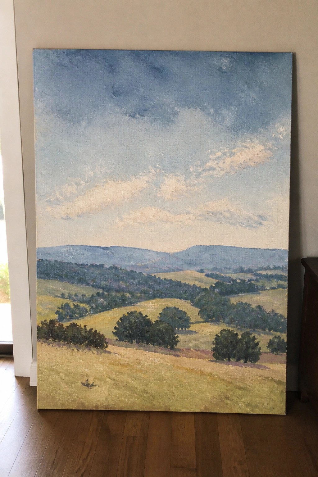Large landscape painting of rolling hills, fields, trees, and blue mountains.