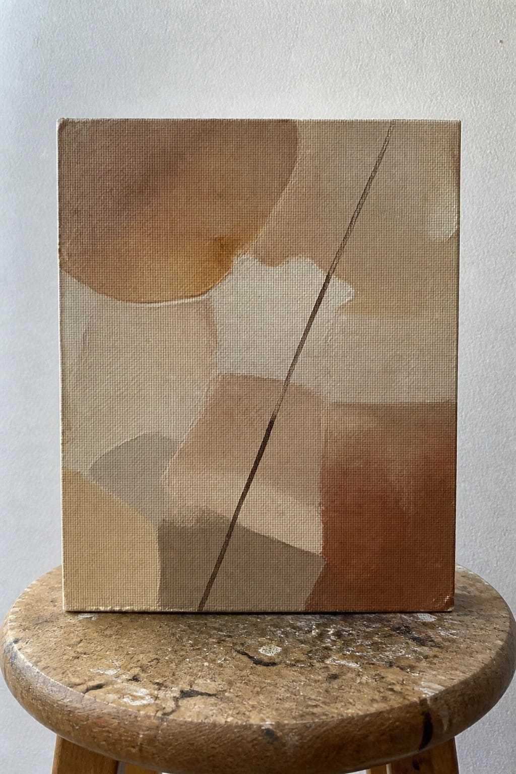 Abstract painting in earthy brown tones on round wooden stool.