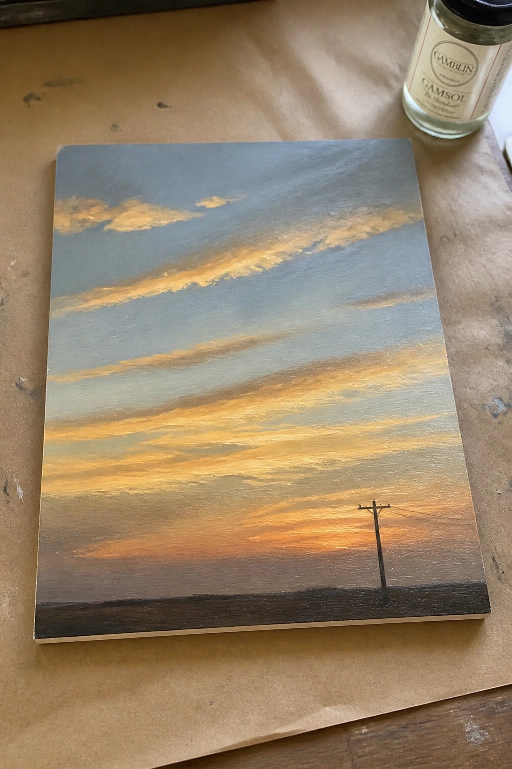 An oil painting of a layered sunset sky in blue, gray, and orange tones with a single utility pole on the right side of a dark horizon.