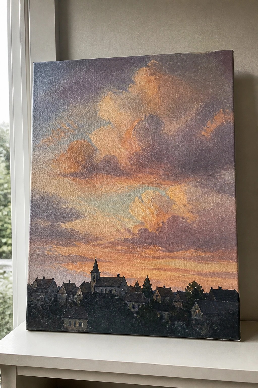 Oil painting of village with church steeple under dramatic orange-purple sunset clouds on windowsill