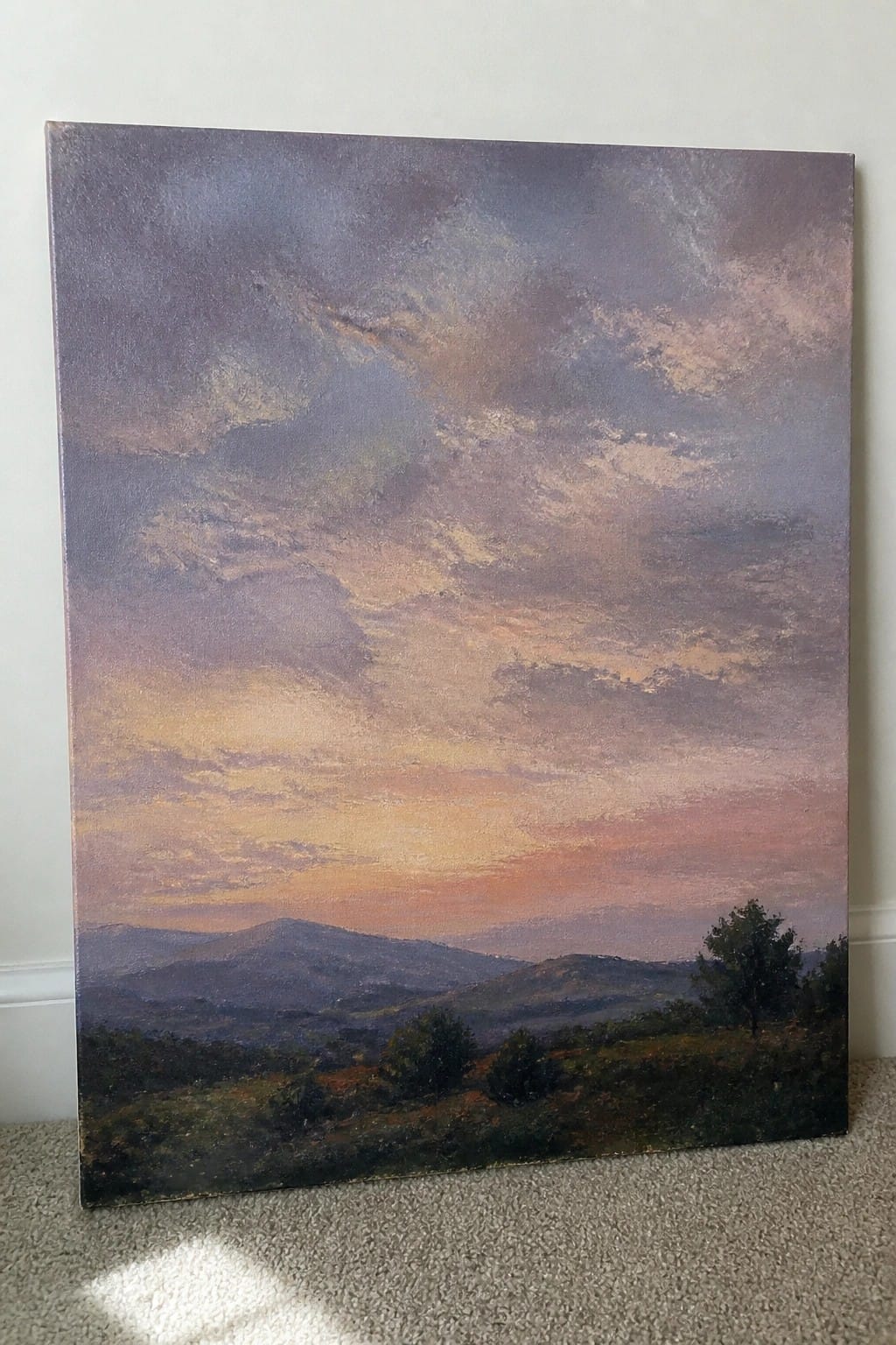 Large canvas landscape painting of sunset over mountains leaning against wall on carpet