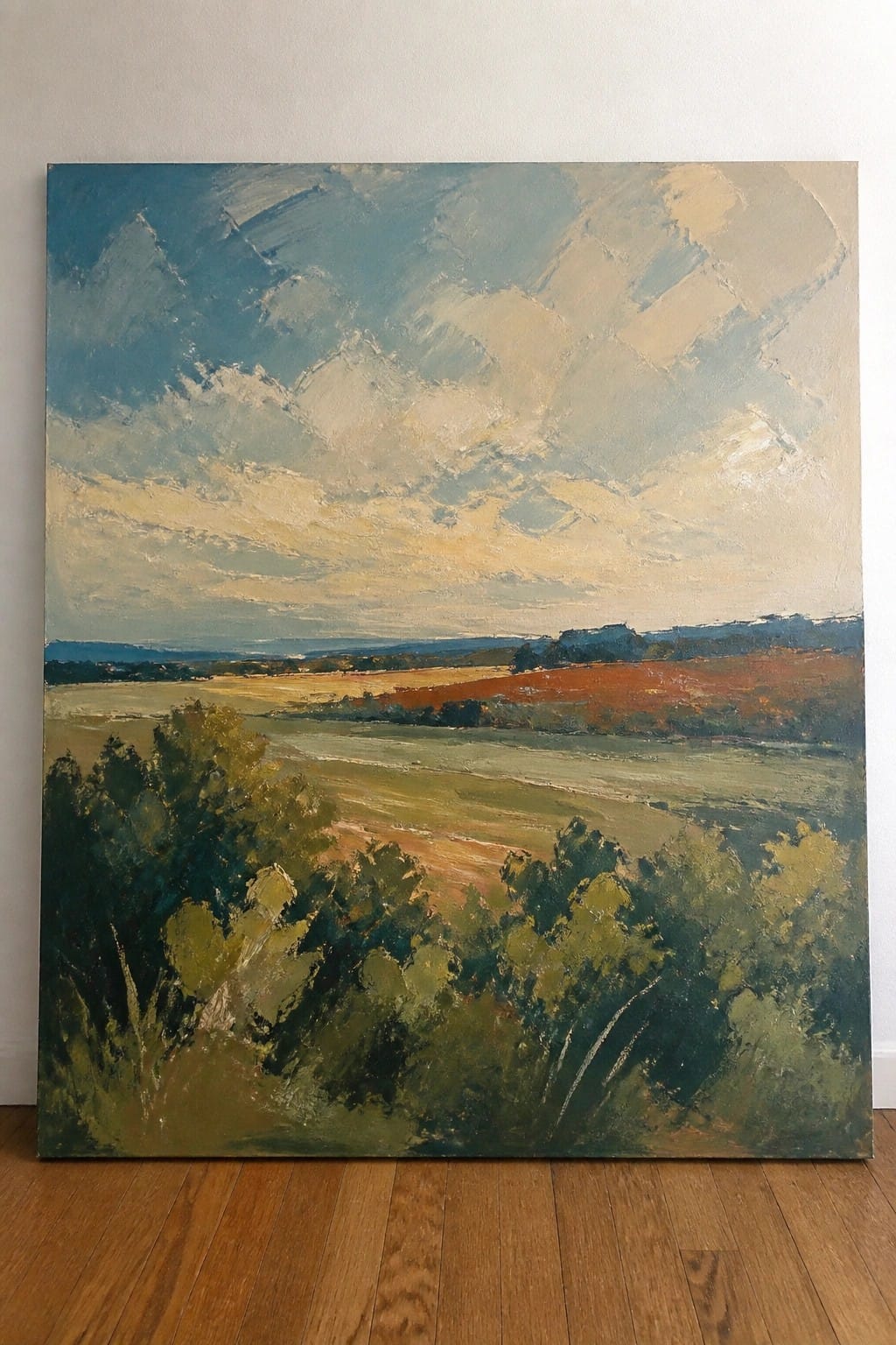 Large landscape painting of fields and cloudy sky leaning on wooden floor