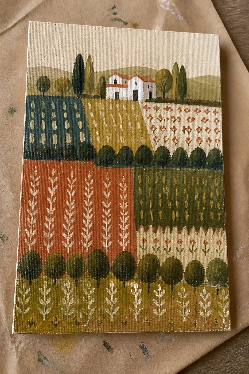 Colorful folk-art landscape with patterned fields, trees, and white houses with red roofs.