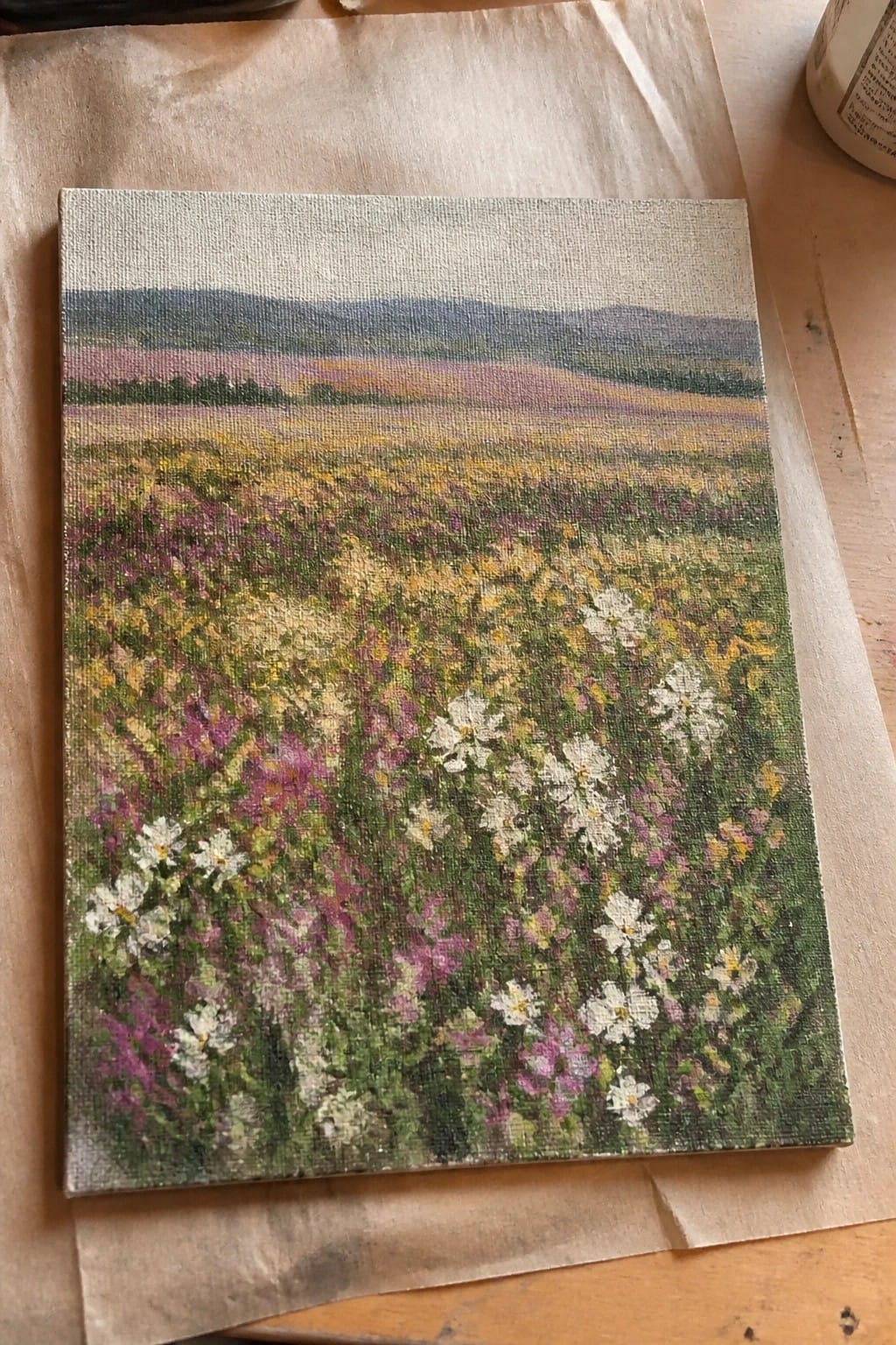 Canvas painting of wildflower meadow with white daisies, colorful blooms, and distant hills