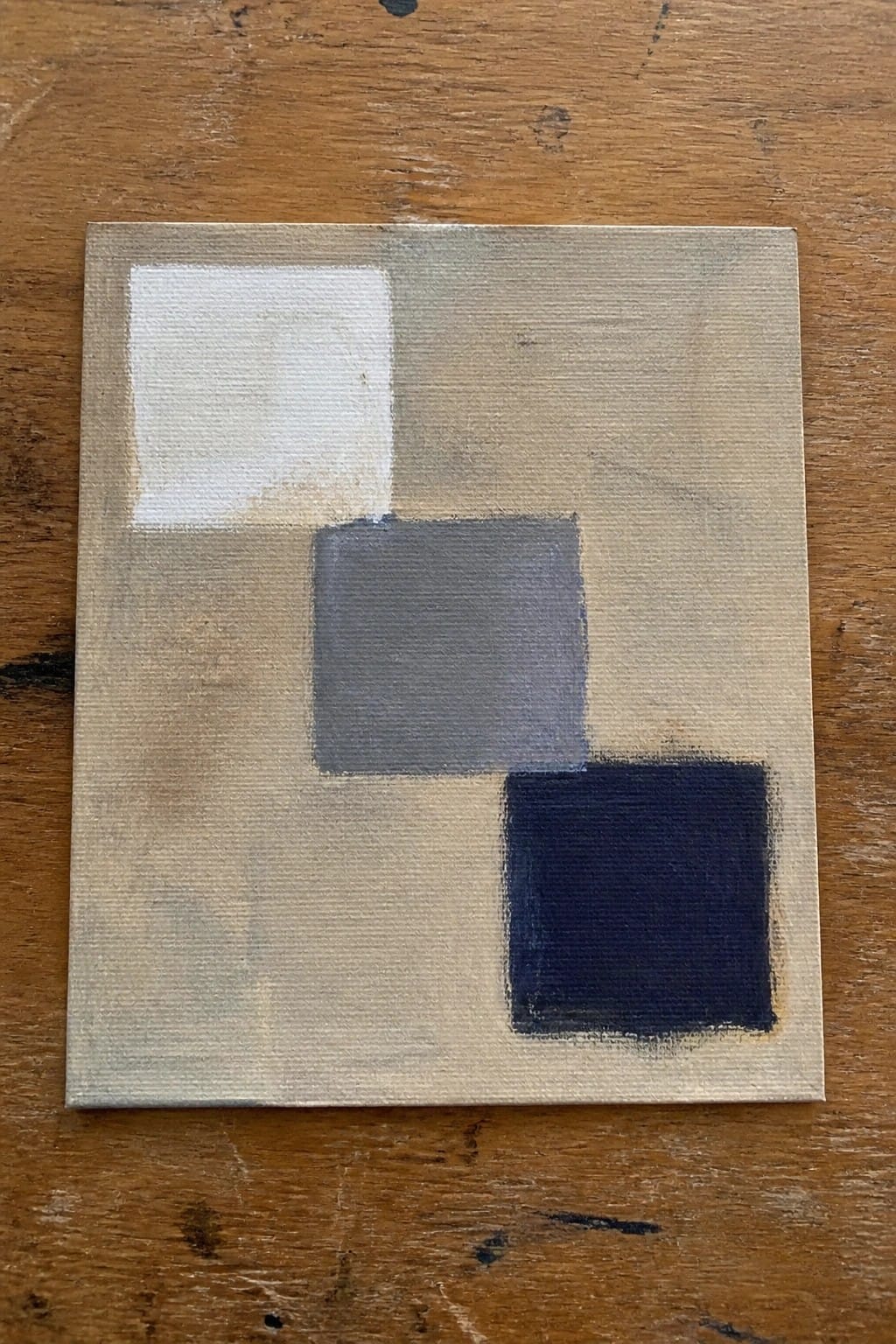 A small oil painting on canvas with three squares in white, gray, and dark blue placed on a beige background.