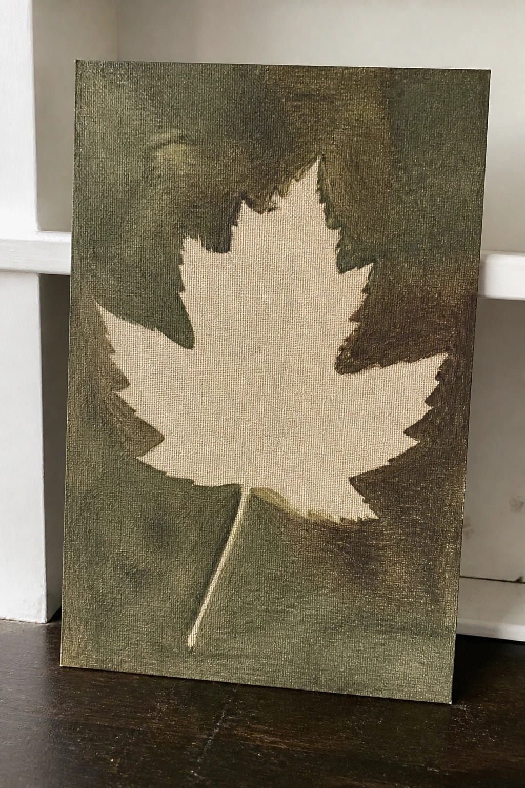 Beige maple leaf painted on dark green textured canvas background resting on wood
