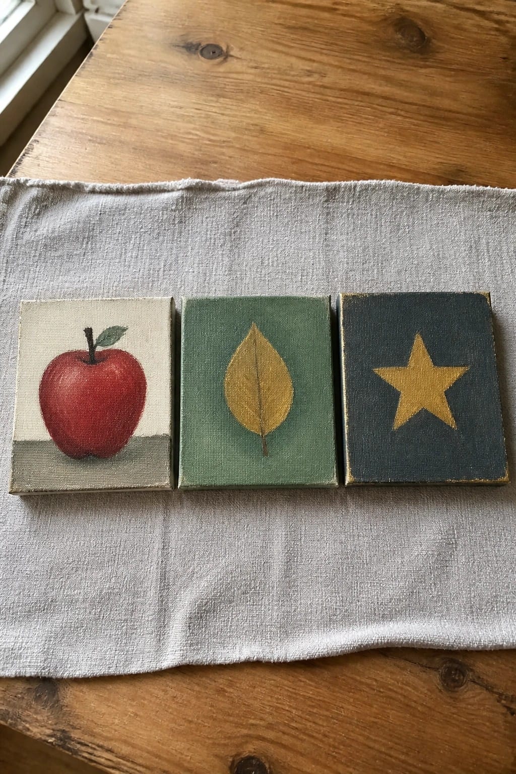 Three small canvases showing a red apple, yellow leaf, and gold star on cloth.