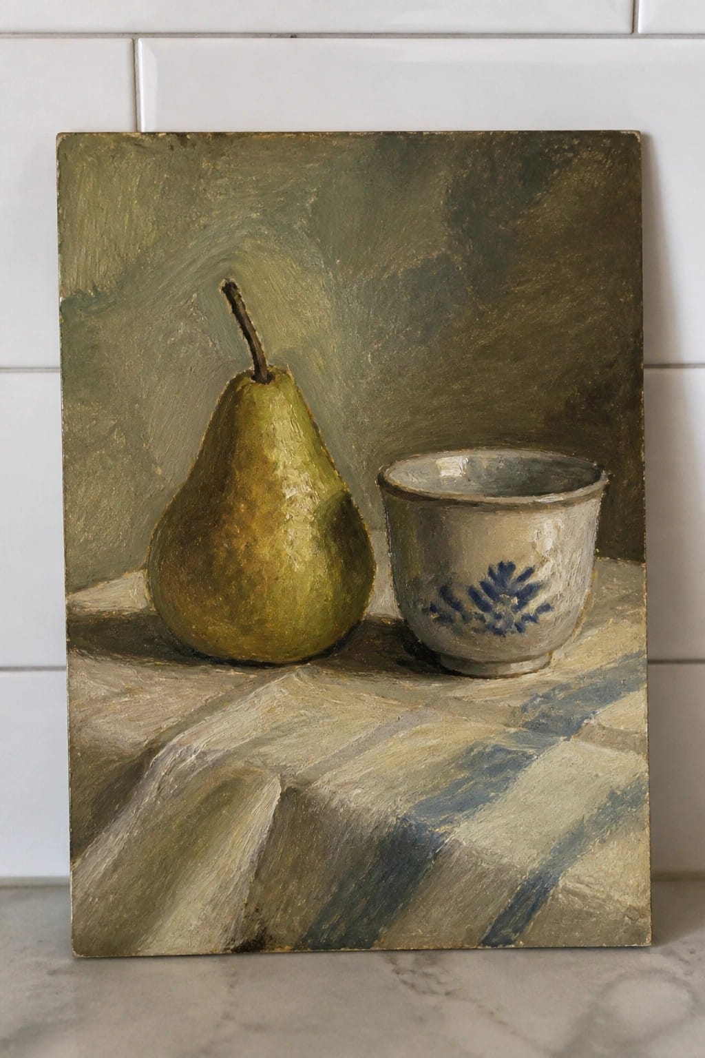 Painting of green pear beside white cup with blue pattern on checkered cloth.