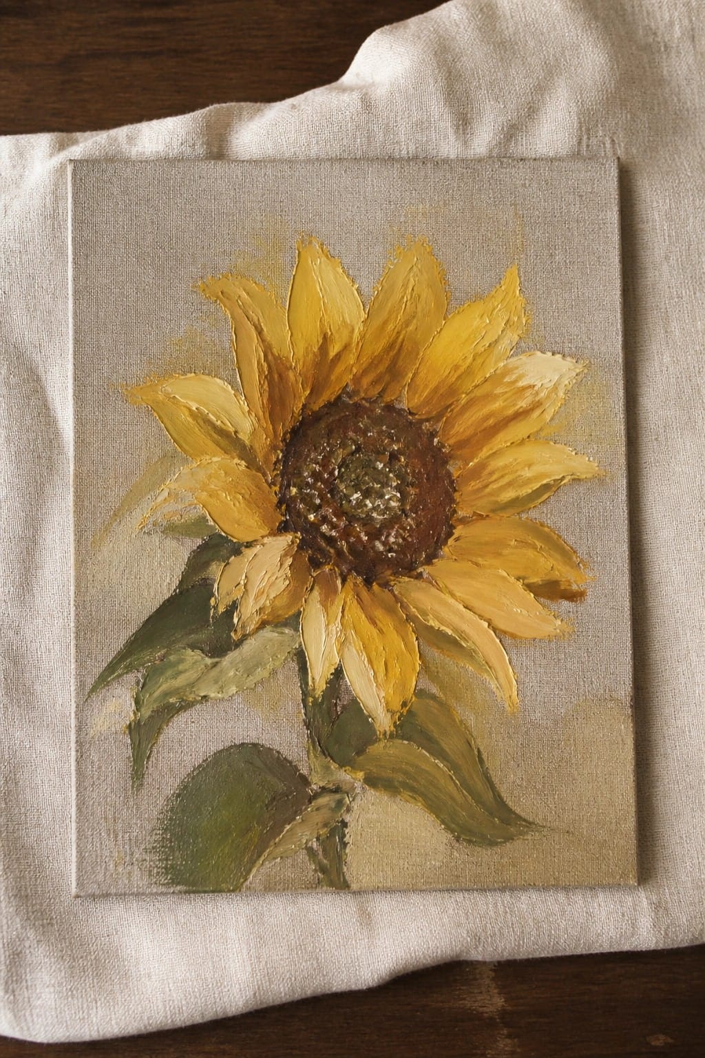 Yellow sunflower oil painting on canvas atop white fabric on wood