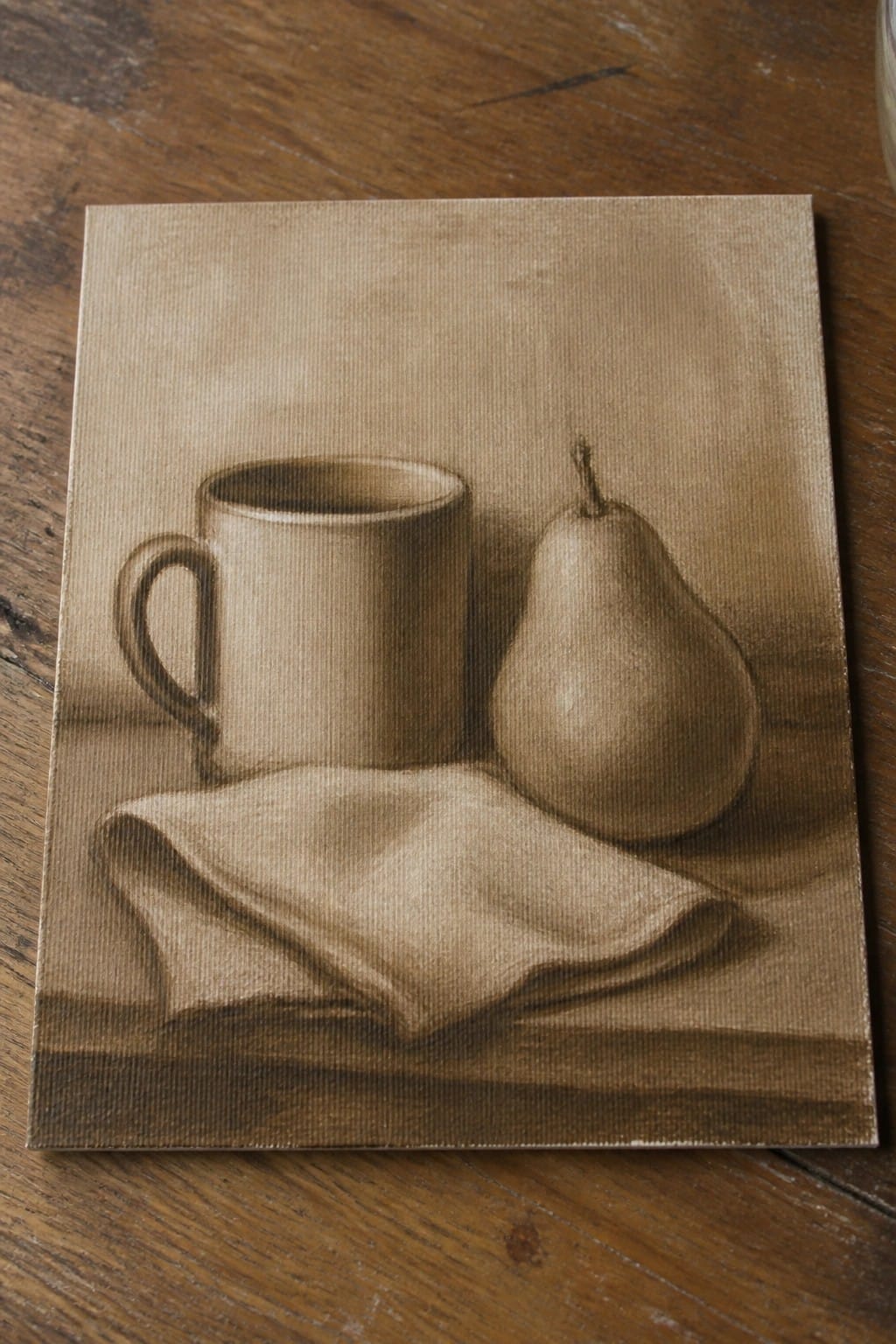 Sepia still life of mug, pear, and folded cloth on wooden surface