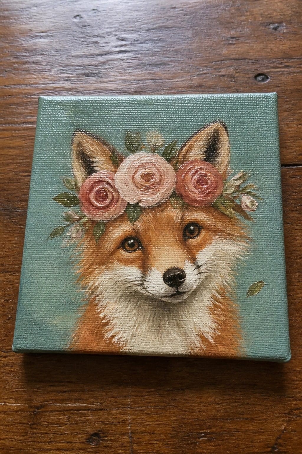 Fox with pink rose crown on teal canvas atop wooden table