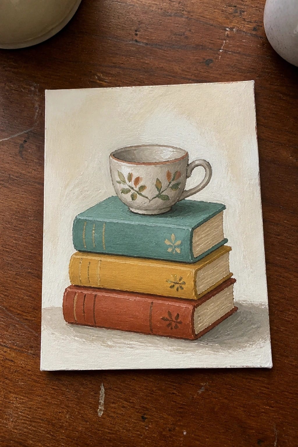 Still life painting of floral teacup atop stacked red, yellow, and teal books.
