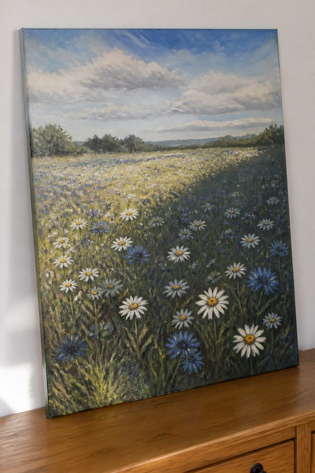 Vibrant meadow painting with white daisies, blue wildflowers, green grass, and cloudy sky