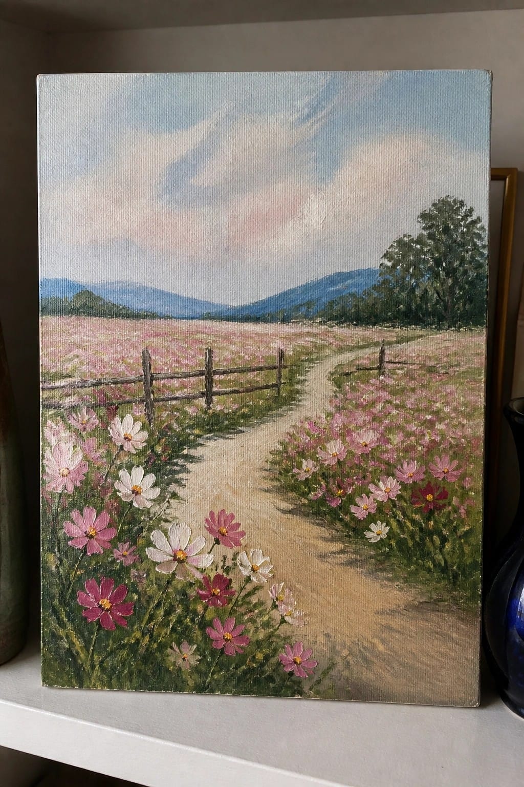 Oil painting of winding path through pink wildflowers, wooden fence, and blue mountains.