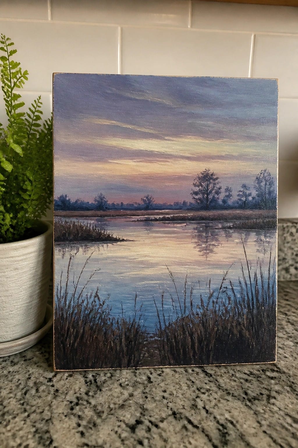 An oil painting of a calm lake at dusk with reeds in the foreground, reflections on the water, and trees under a colorful sky.