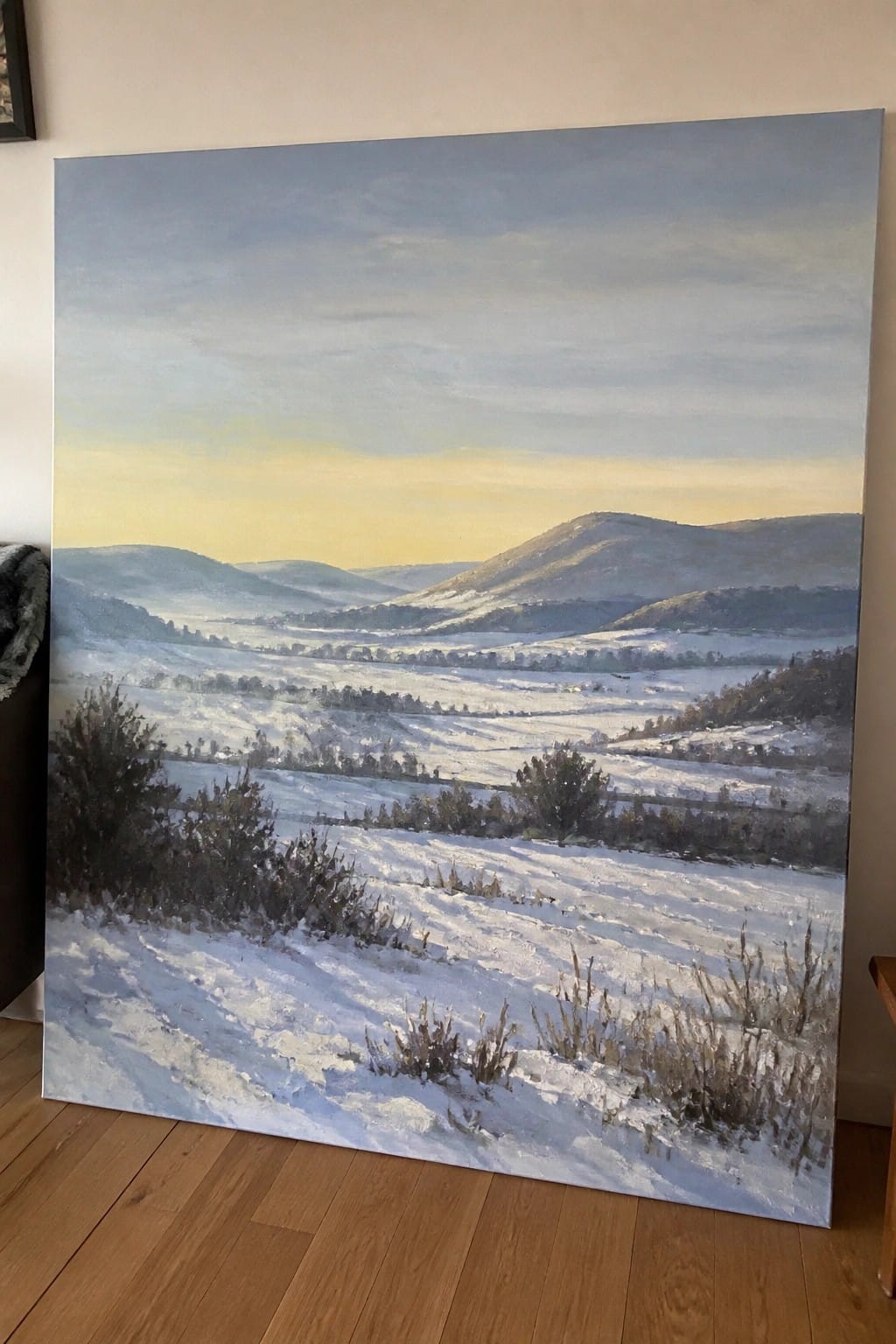 An oil painting of a broad snowy valley with rolling hills and distant mountains beneath a soft blue and yellow sky.