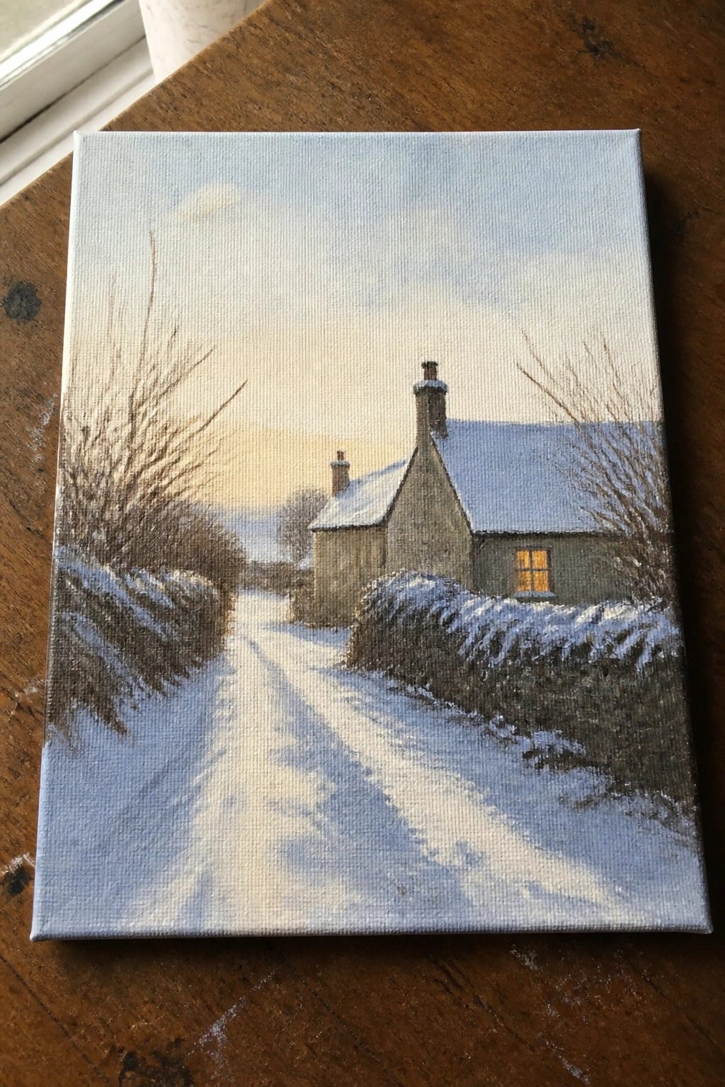 Snow-covered cottage with glowing window beside winding snowy path at dusk