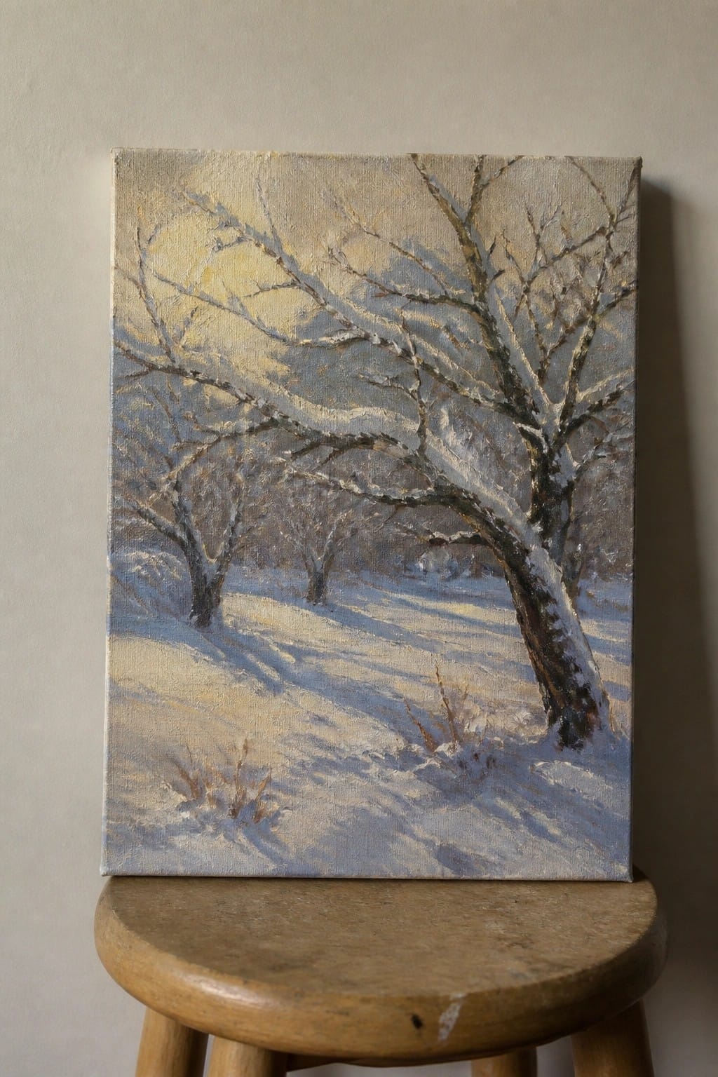 Oil painting of snow-covered trees in a sunlit winter landscape on a wooden stool.