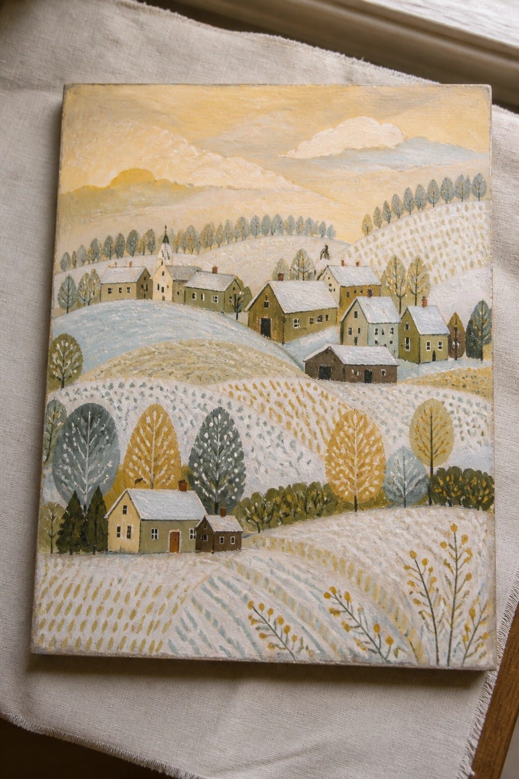 Folk art painting of snowy village houses on rolling hills with colorful trees.