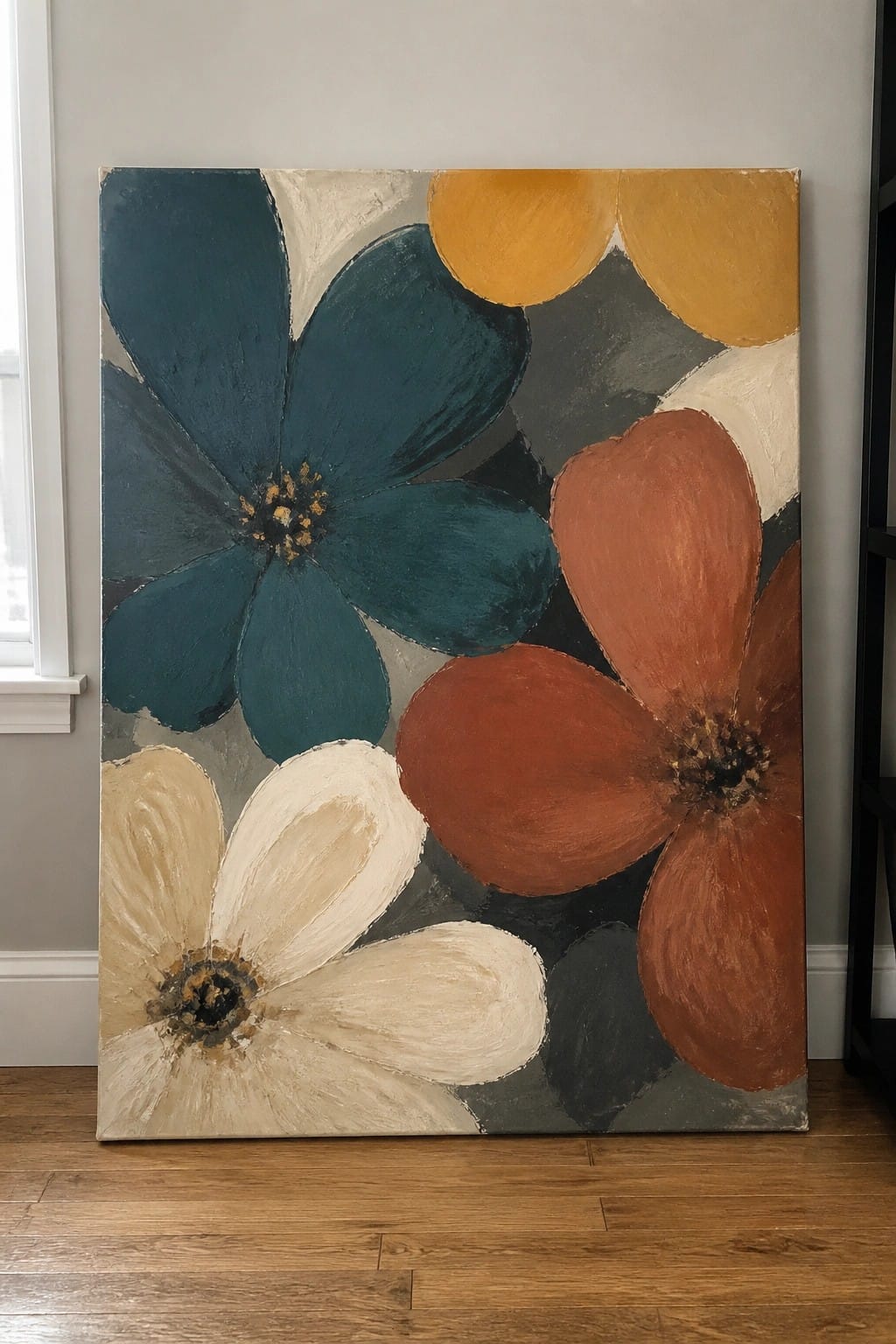 Large abstract oil painting of overlapping flowers in teal, rust, cream, and yellow on a gray background, leaning against a wall above a wooden floor.