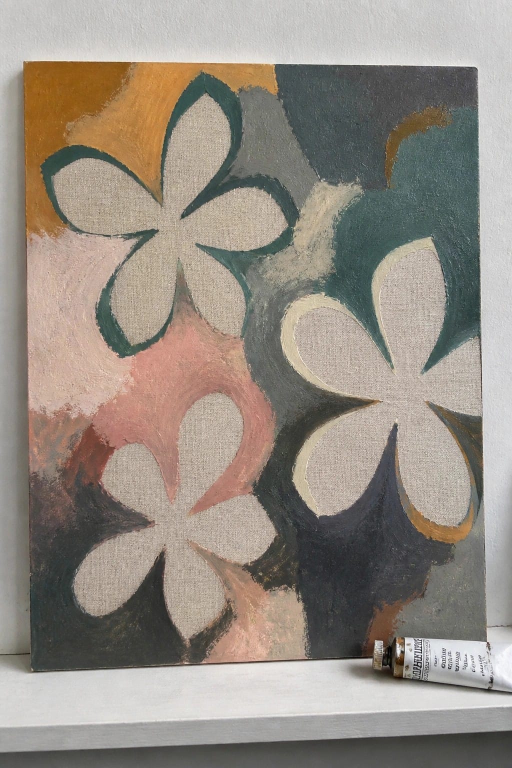 Abstract painting of beige flowers on colorful background beside paint tube on shelf