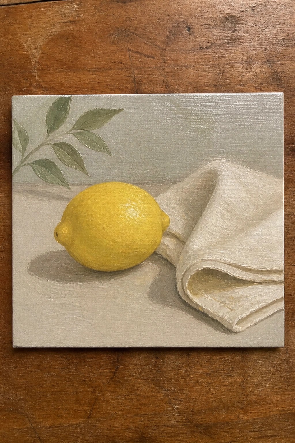 Yellow lemon beside white folded cloth with green leaves on gray surface
