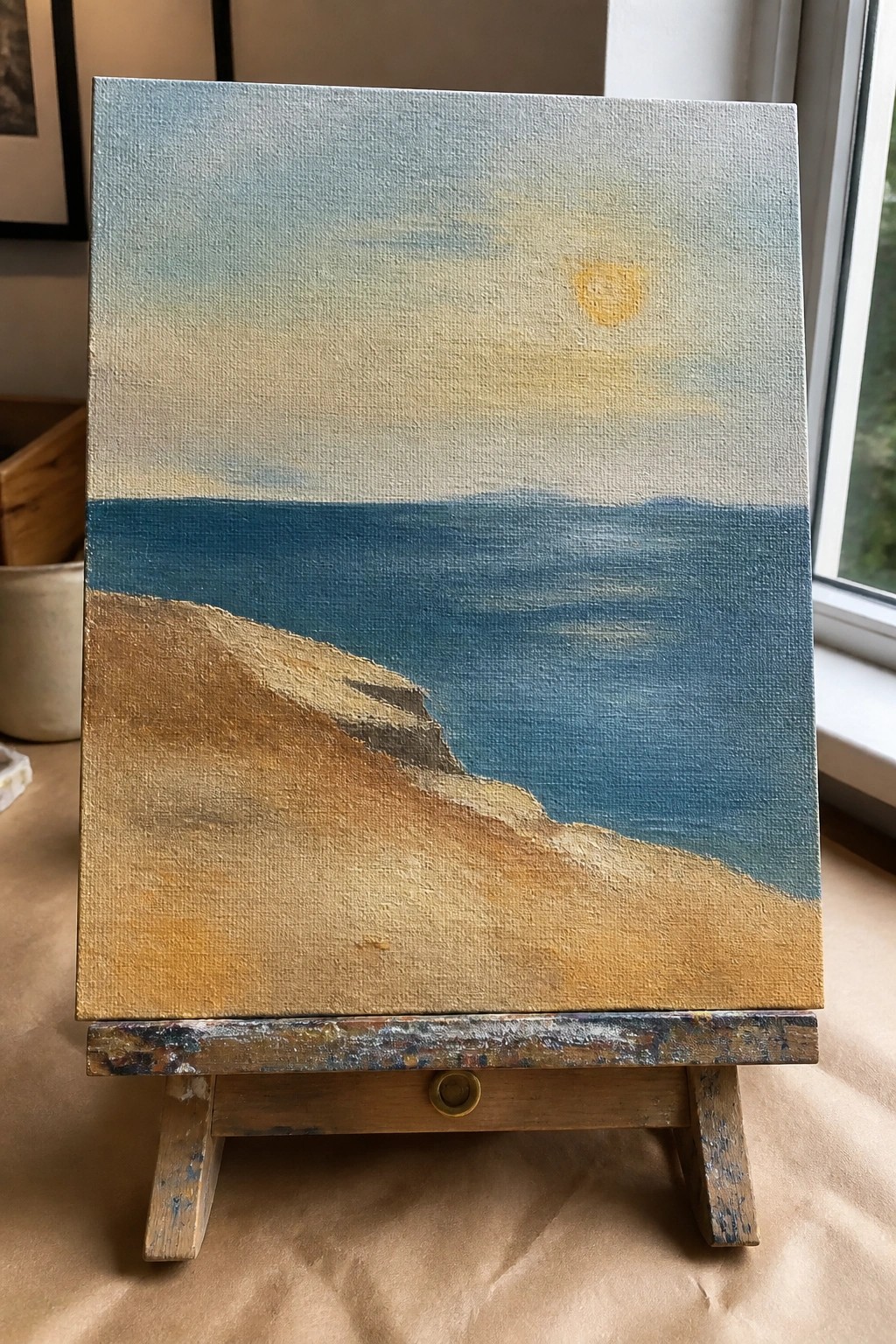 Oil painting of sandy beach and blue ocean under sun on wooden easel