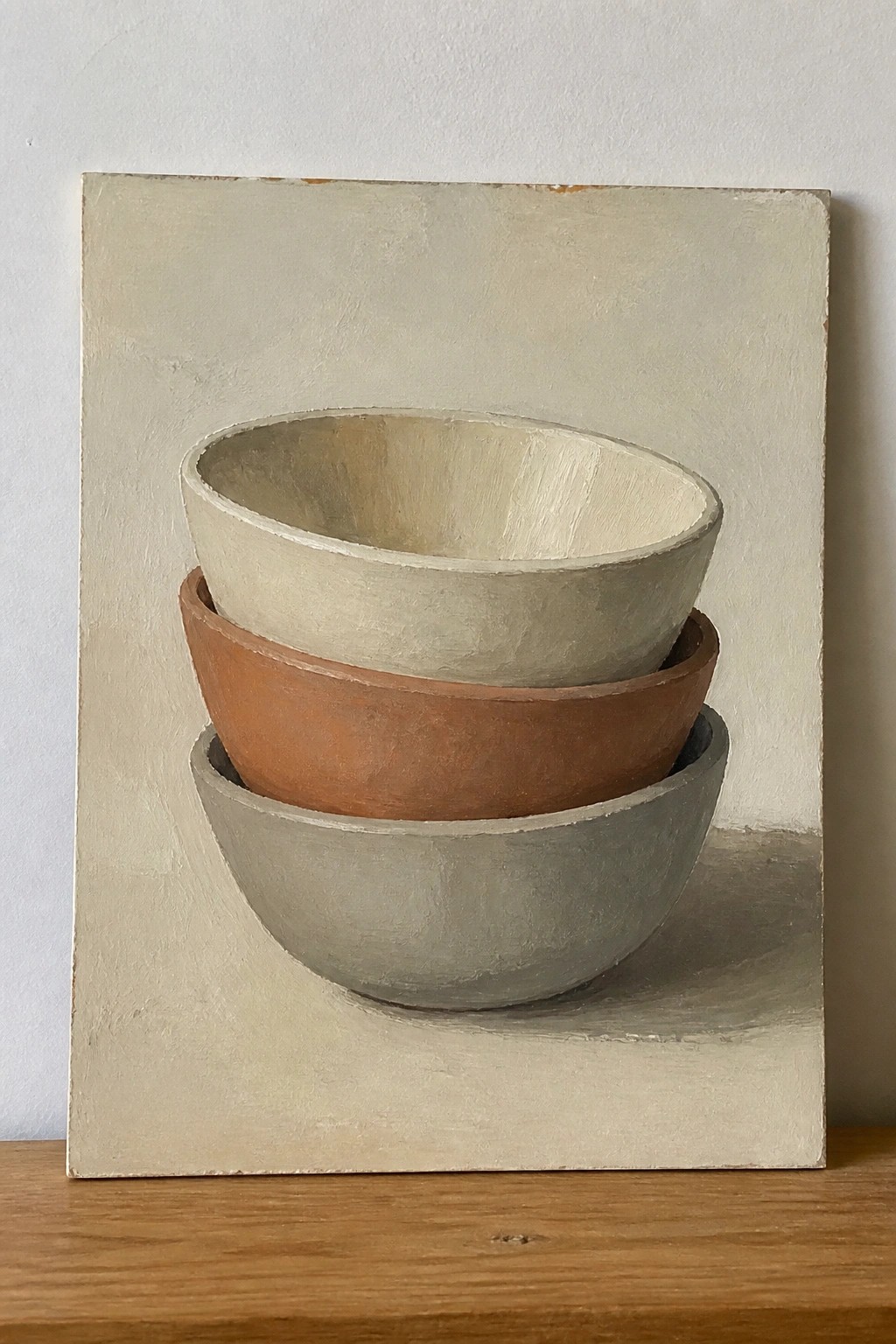 Three stacked bowls in white, terracotta, and gray on a wooden surface