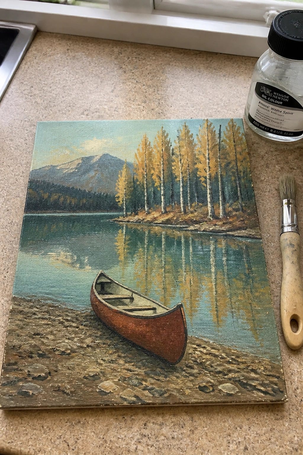 Landscape painting of red canoe on lakeshore with autumn trees, mountains and reflections