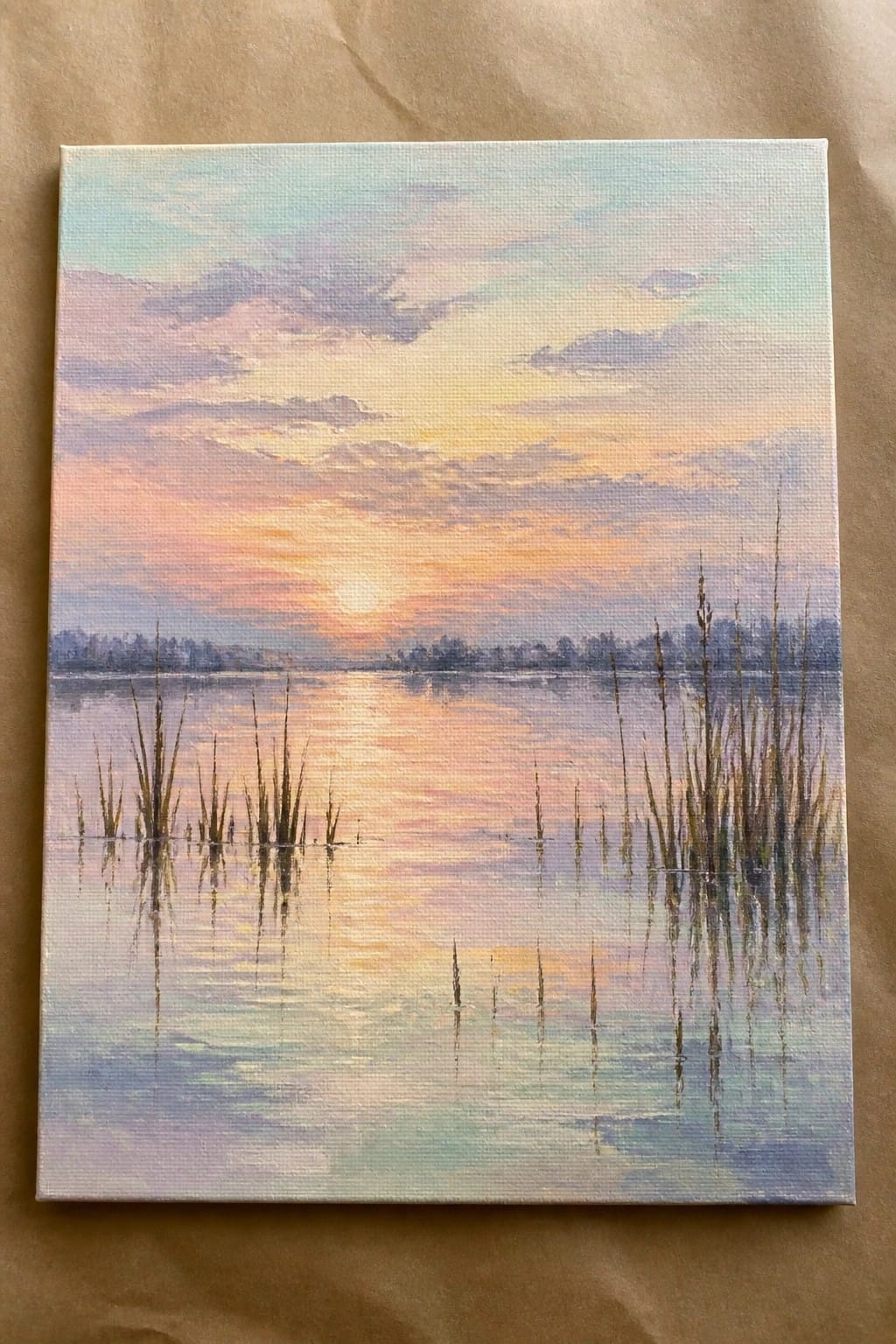 Pastel sunset painting with colorful sky, calm water, and tall reeds reflecting.