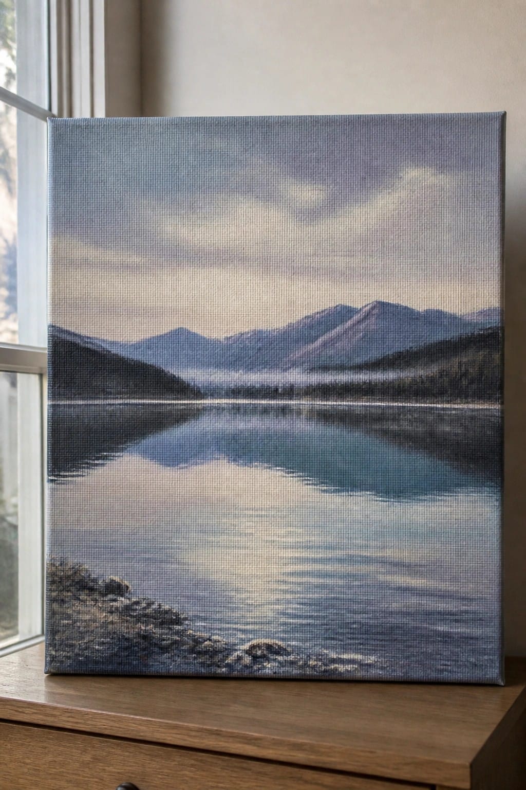 Canvas painting of misty mountains reflected in calm blue lake by window