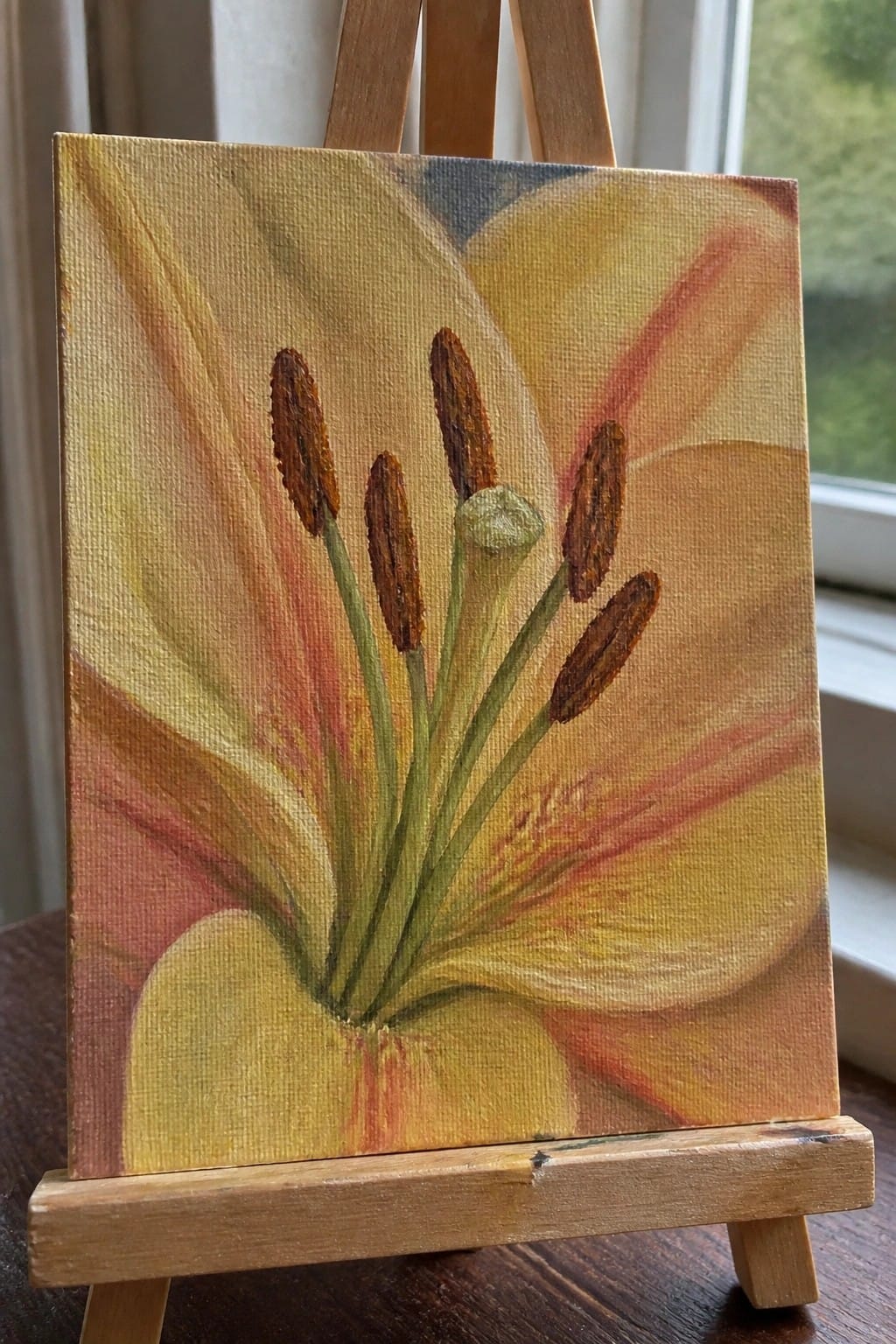 Yellow-orange lily painting with brown stamens on small wooden easel by window